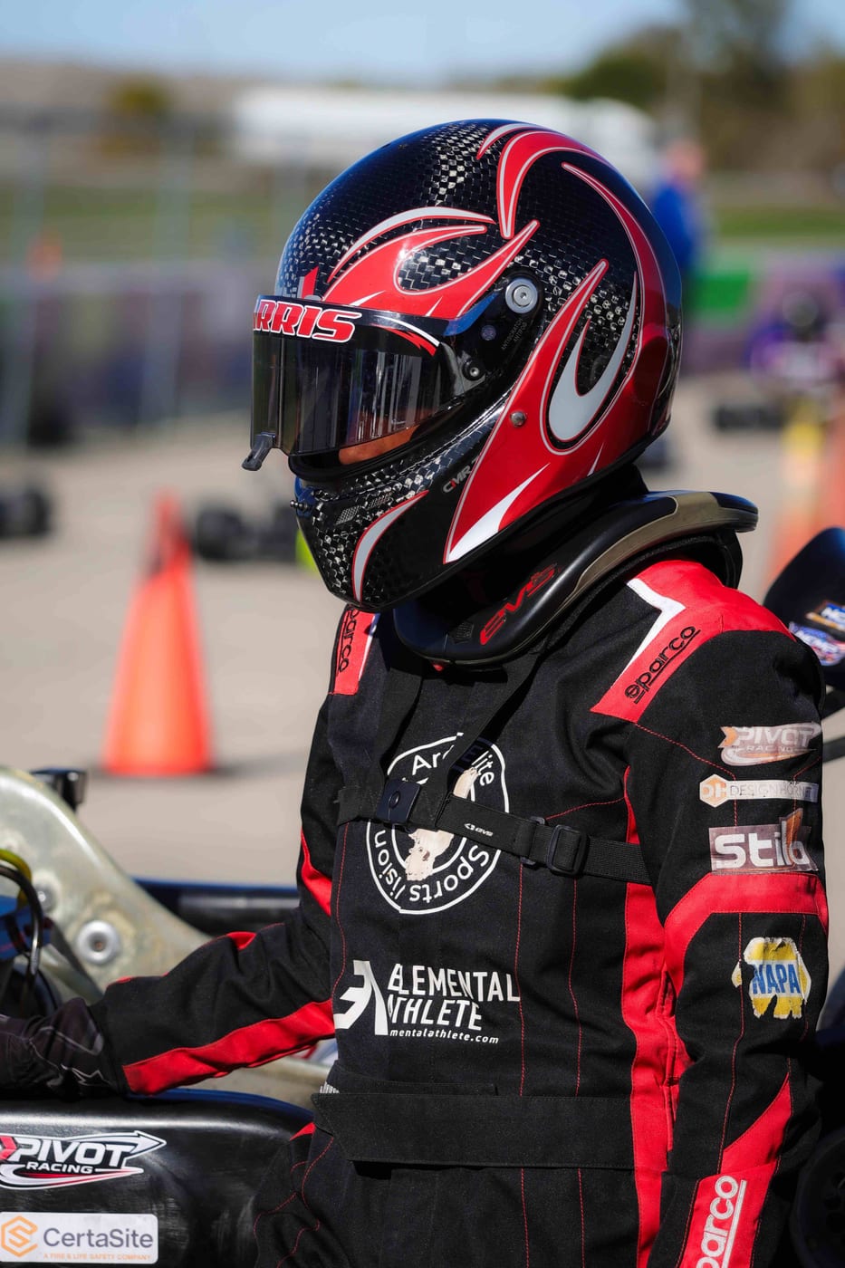 Pivot Racing driver Asher Farris in his red and black carbon helmet and Sparco race suit beside his kart