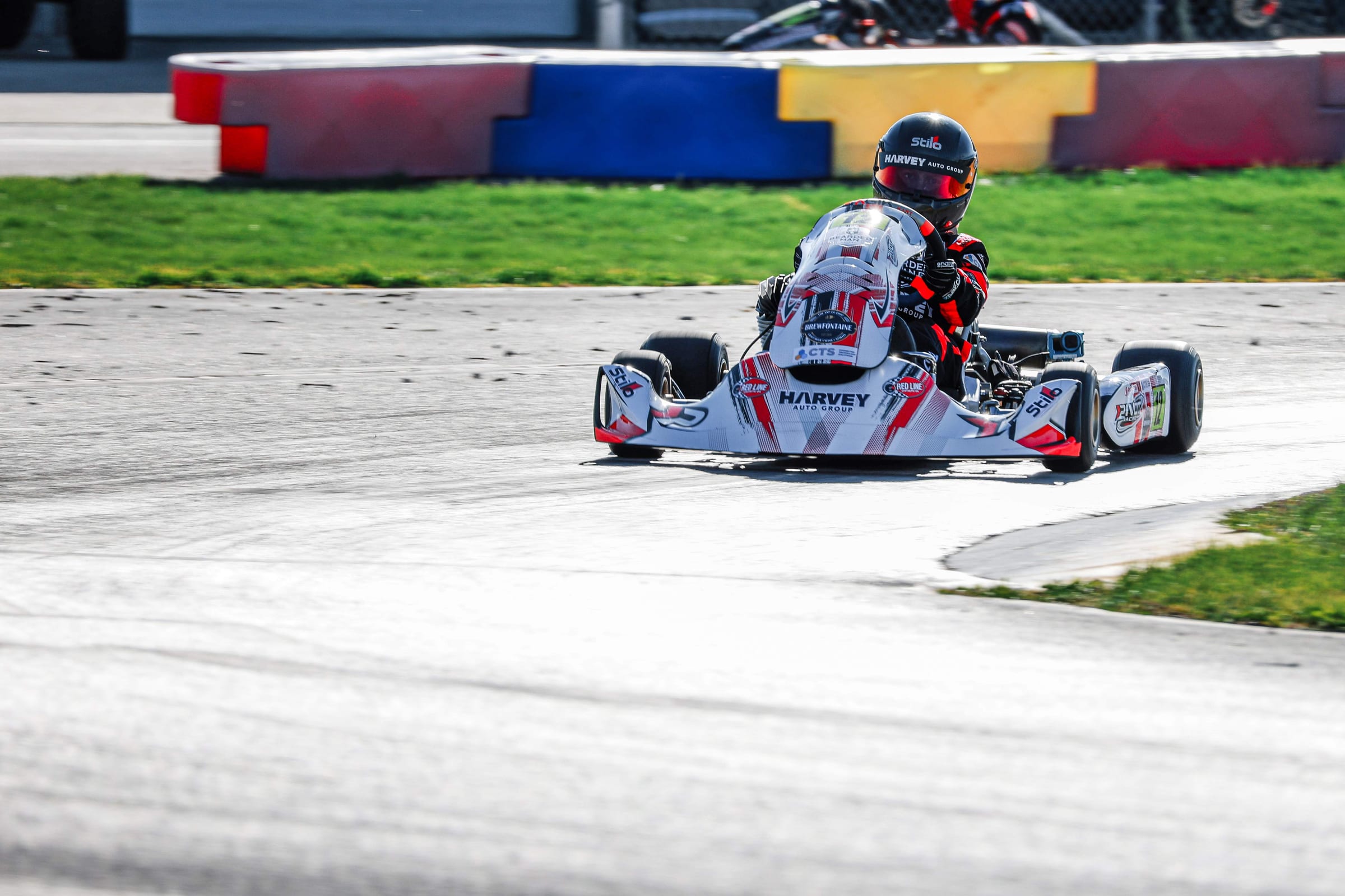 A Pivot Racing driver cornering in a red and white kart on track