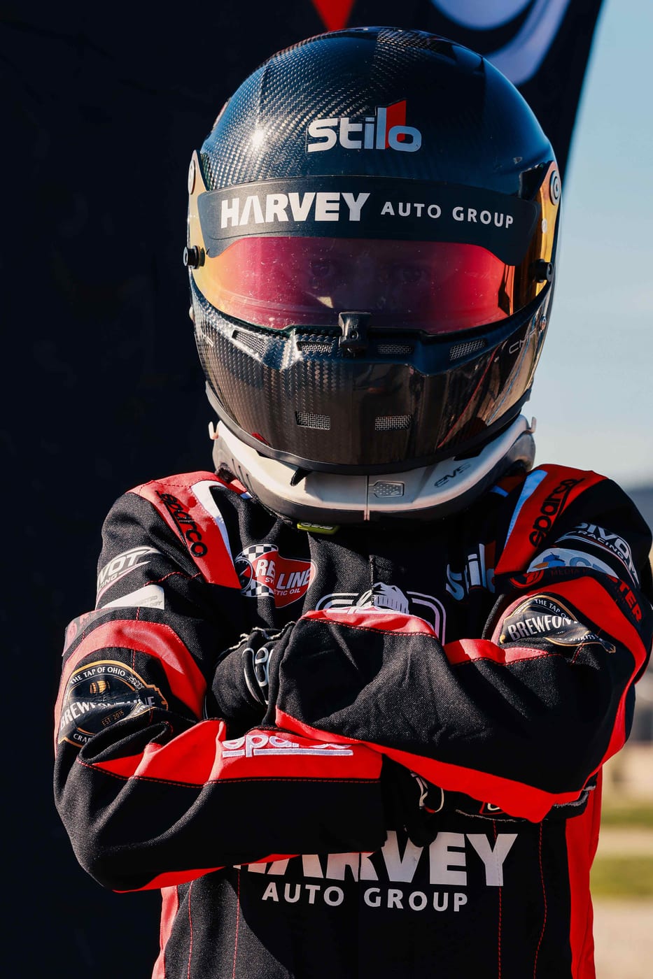 Pivot Racing driver Jerome Wickham in a carbon fiber Stilo helmet and red and black race suit with arms crossed
